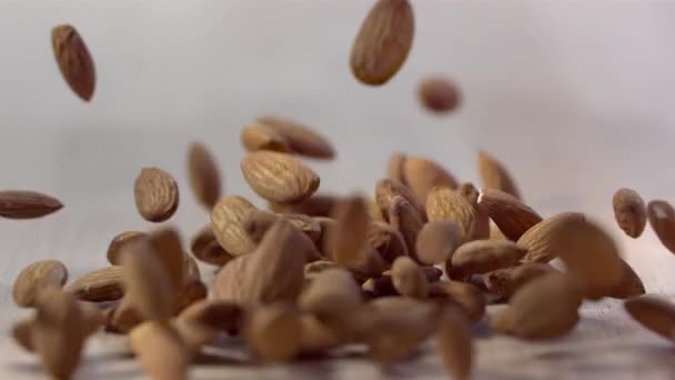 Pile of almond nuts falling down on wooden surface, slow motion - Filmati, video
