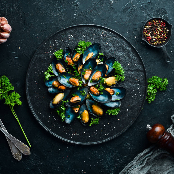 Boiled mussels with parsley and spices on a black plate. Top view. Free space for your text. - Фото, изображение