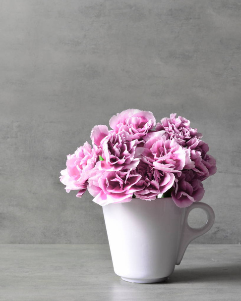 灰色の背景にカップにピンクのカーネーションの花. - 写真・画像