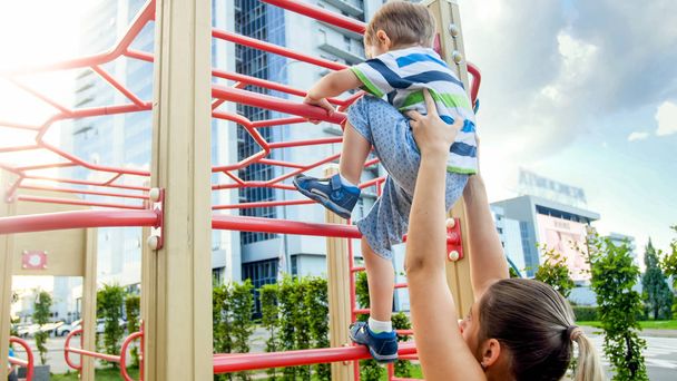 Closeup image of young mother helping her little son climbing on high metal stairs at sports children playground - Fotografie, Obrázek