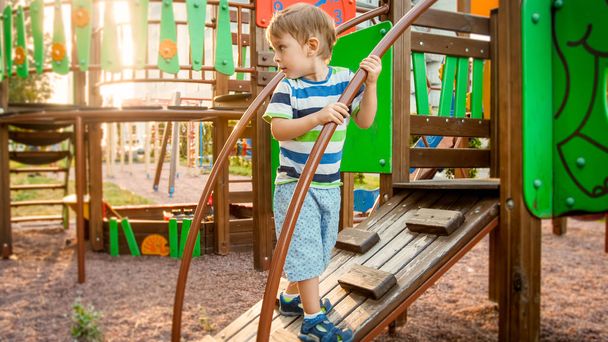 Portret aktywnego małego chłopca pełzające i wspinaczka na drewnianych schodach na plac zabaw dla dzieci w parku - Zdjęcie, obraz