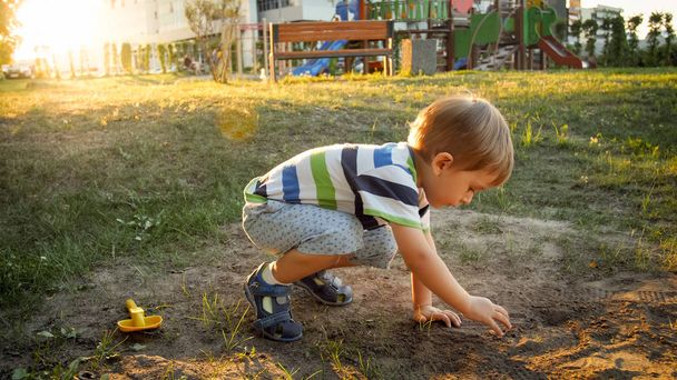 Foto von 3-jährigem kleinen Jungen, der auf dem Boden im Park sitzt und Sand gräbt - Foto, Bild