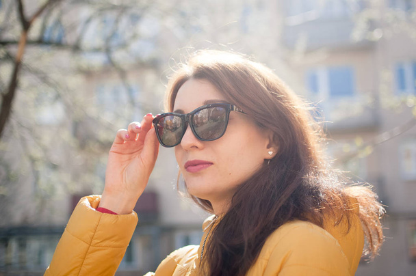 Menina alegre bonita com lábios sensuais usando óculos de sol enquanto desfruta da primavera na cidade
. - Foto, Imagem