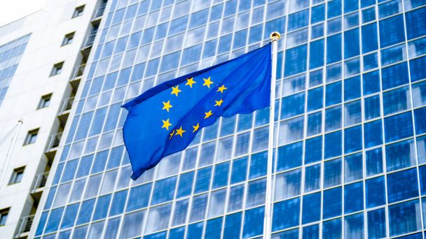Wizerunek flagi UE trzepotanie na wiatr przed wysokim biurowym budynku biznesowym z concerete i szkła. Koncepcja ekenomiki, rozwoju, rządu i polityki - Zdjęcie, obraz