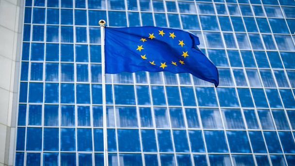 Obraz vlajky EU se třepetá ve větru před budovou vysoké podnikatelské kanceláře, která je vyrobena z harmonete a skla. Koncepce ekenomiky, rozvoje, vlády a politiky - Fotografie, Obrázek