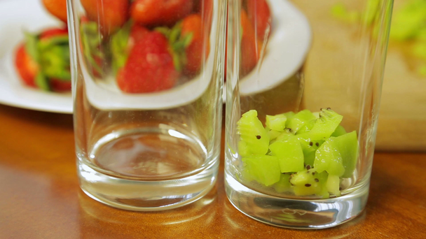 A woman puts a piece of green kiwi in a cocktail glass - Footage, Video
