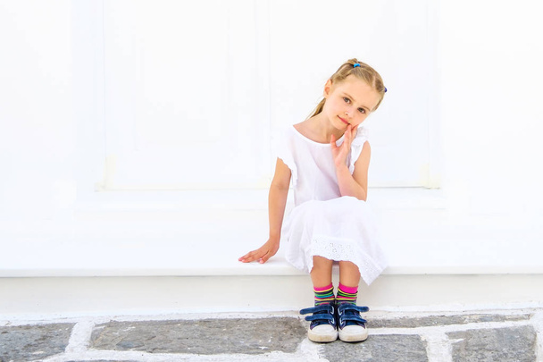 Little pretty blong girl in a white dress sitting outdoor - Fotó, kép