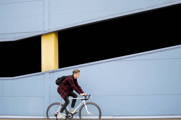 jeune gars élégant monte un vélo blanc vers l'avant sur un fond de mur bleu
 - Photo, image