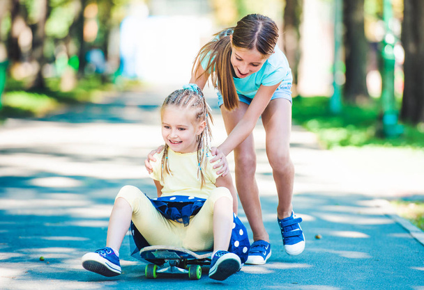 Smiling kids riding on skateboard in park - Zdjęcie, obraz