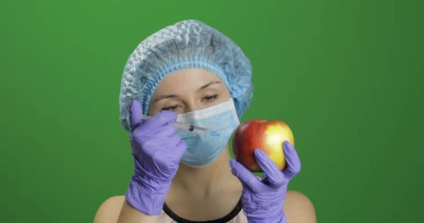 Kobieta naukowiec wykonuje wstrzyknięcie za pomocą strzykawki medycznej w jabłkach - Zdjęcie, obraz