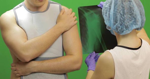 Άνθρωπος με τραυματισμό στον ώμο. Η νοσοκόμα εξετάζει ακτίνες χ. Επίδεσμος για τη στερέωση του ώμου - Φωτογραφία, εικόνα