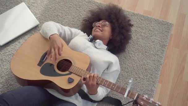 Όμορφη αφρικανική Αμερικανίδα γυναίκα με ένα Άφρο χτένισμα που βρίσκεται στο πάτωμα παίζοντας κιθάρα πάνω όψη - Πλάνα, βίντεο