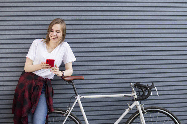 joven hermosa chica de pie con una bicicleta en el fondo de una pared y mira en el teléfono, una mujer descansa de un viaje
 - Foto, imagen