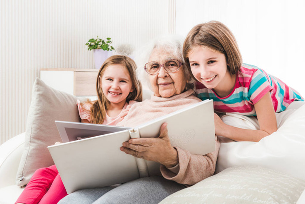 Бабушка с внучками ищет семейный фотоальбом
 - Фото, изображение