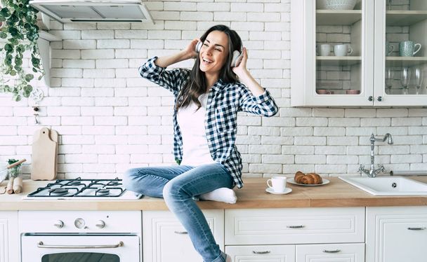 Relax at home. Beautiful happy young woman in headphones is listening music and have a fun on the kitchen. - Foto, imagen