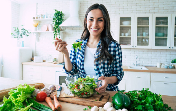 Healthy lifestyle. Good life. Organic food. Vegetables. Close up portrait of happy cute beautiful young woman while she try tasty vegan salad in the kitchen at home. - Φωτογραφία, εικόνα