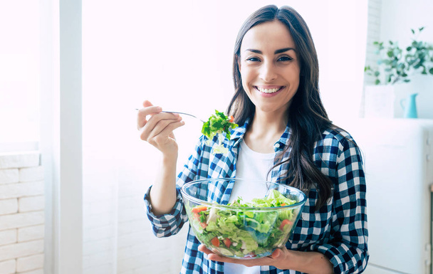 Healthy lifestyle. Good life. Organic food. Vegetables. Close up portrait of happy cute beautiful young woman while she try tasty vegan salad in the kitchen at home. - Foto, immagini
