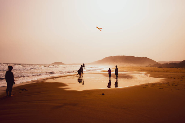 Silhouettes of people playing and flying a kite in sandy Golden  - Photo, Image