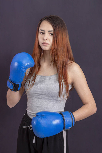 boxer girl in blue boxing gloves in a gray t-shirt in the rack - Zdjęcie, obraz