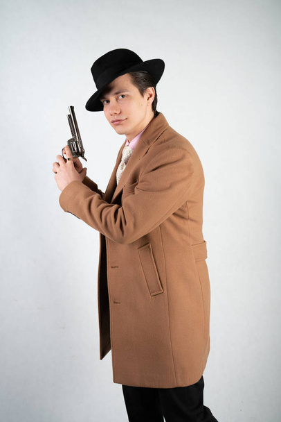 Young man in a formal suit and hat with a gun in his hands on a white background in the Studio alone isolated - Fotoğraf, Görsel