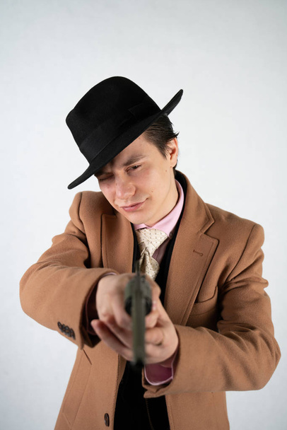Jeune homme dans un costume formel et chapeau avec un pistolet dans les mains sur un fond blanc dans le studio seul isolé
 - Photo, image