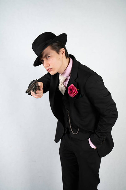 joven con un traje formal y un sombrero con una pistola en las manos sobre un fondo blanco solo en el estudio
 - Foto, imagen