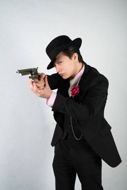 mladý muž ve formálním obleku a klobouku s pistolí v ruce na bílém pozadí studia samotného - Fotografie, Obrázek