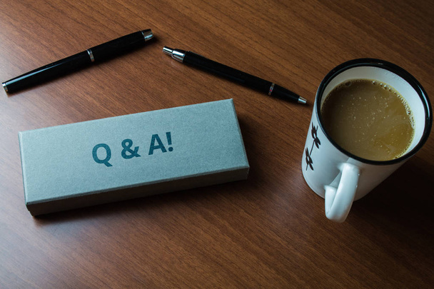 Tekst do pisania słów Q i A. Biznes koncepcja zdefiniowana jako pytania i odpowiedzi Górny widok bliski dwa długopisy przypadku zestaw filiżanka kawy leżąca drewniany stół. - Zdjęcie, obraz