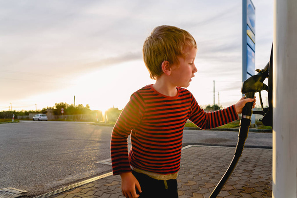 ガソリンスタンドで日没時に燃料ポンプのホースを持つ子供 - 写真・画像