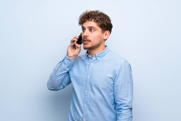 Uomo biondo oltre il muro blu mantenere una conversazione con il telefono cellulare
 - Foto, immagini