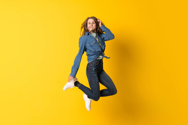 Young woman jumping over yellow background - Foto, afbeelding