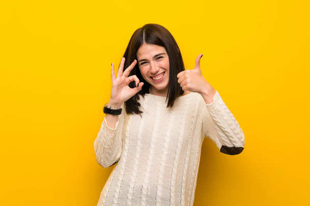 Young woman over isolated yellow wall showing ok sign and thumb up gesture - Photo, Image