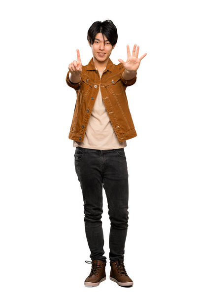 A full-length shot of a Asian man with brown jacket counting six with fingers over isolated white background - Photo, Image