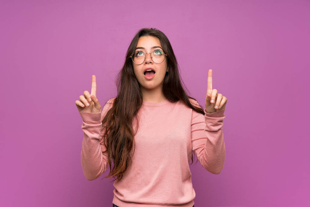 Teenager girl over purple wall surprised and pointing up - Photo, Image