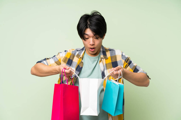 Asiatique homme sur mur vert isolé tenant beaucoup de sacs à provisions
 - Photo, image