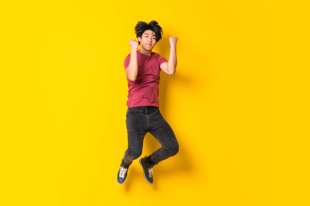 Asian man jumping over isolated yellow wall - Fotó, kép