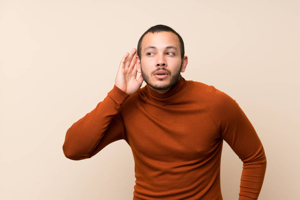 Colombian man with turtleneck sweater listening to something by putting hand on the ear - Photo, Image