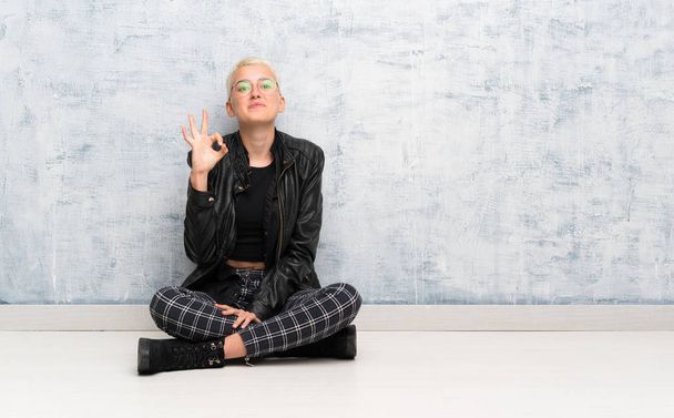 Jeune femme assise sur le sol montrant ok signe avec les doigts - Photo, image