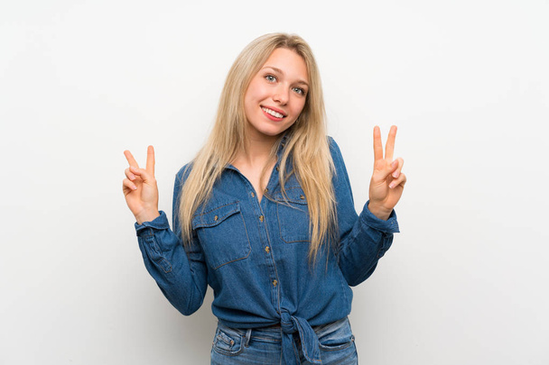 Young blonde woman over isolated white wall showing victory sign with both hands - Zdjęcie, obraz