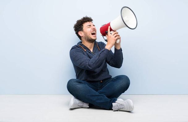 Young man sitting on the floor shouting through a megaphone - Photo, Image