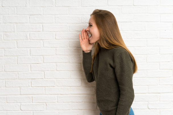 Fiatal nő több mint fehér téglafal kiabálva száj tárva-nyitva - Fotó, kép