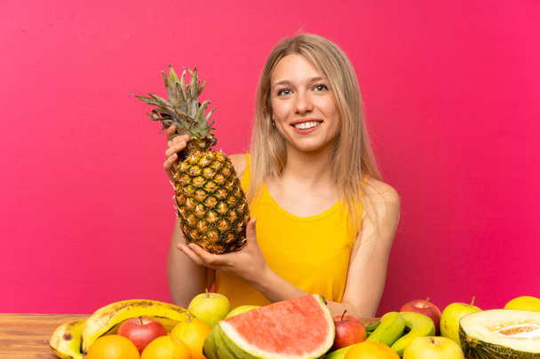 Νεαρή γυναίκα με πολλά φρούτα που κρατάνε έναν ανανά - Φωτογραφία, εικόνα