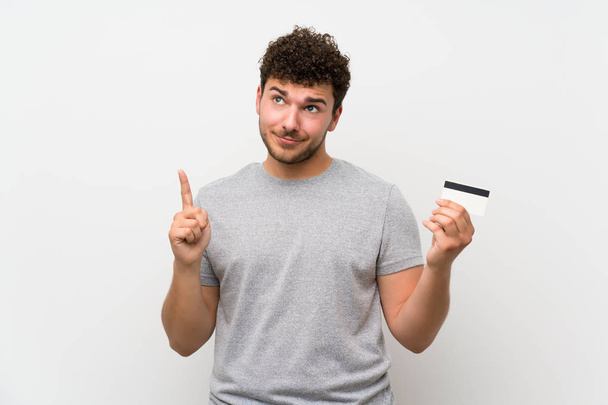 Mann mit lockigem Haar über isolierter Wand mit Kreditkarte - Foto, Bild