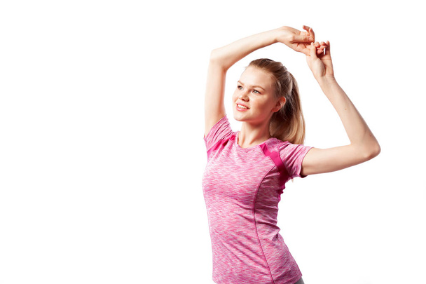 Uma jovem mulher atleta magro em um top esportivo rosa levantou as mãos para cima e fazendo um exercício para bíceps, esticando-se em um fundo isolado branco no estúdio. Retrato de uma bela mulher do esporte
 - Foto, Imagem