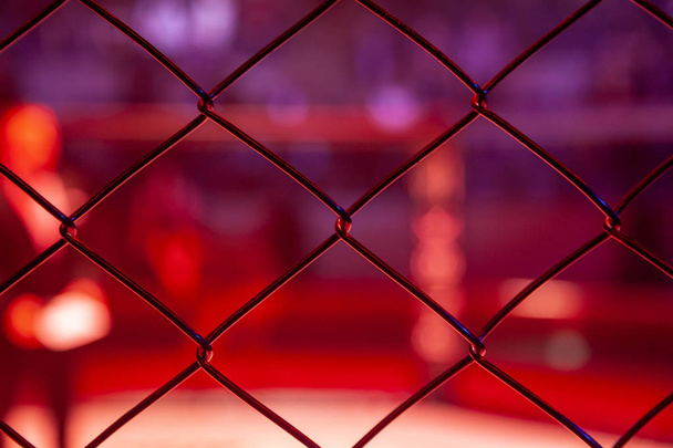 Boks prowadzący przed walką na arenie ośmiokątne sceny, widok przez metalową siatkę. Człowiek w sporcie mieszanych sztuk walki w zawodach MMA. - Zdjęcie, obraz