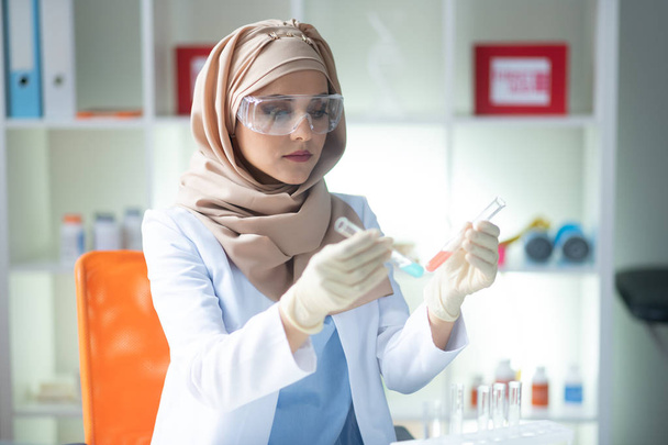 Young female chemist wearing white gloves holding test tubes - 写真・画像