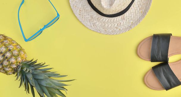 Widok z góry na kobiecej sandale słomkowy kapelusz, Okulary przeciwsłoneczne i ananas na żółtym tle  - Zdjęcie, obraz