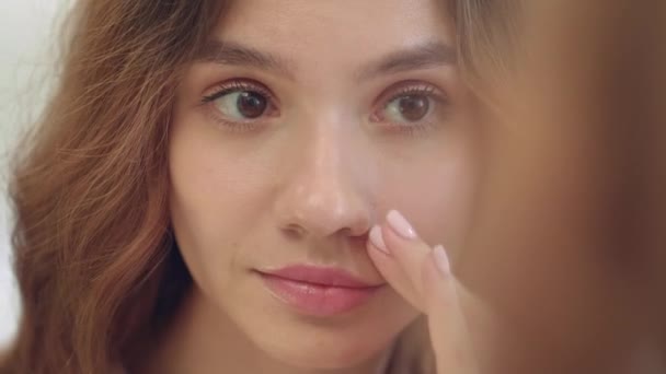 Smiling woman applying moisturizing cream on face skin front bathroom mirror - Кадры, видео