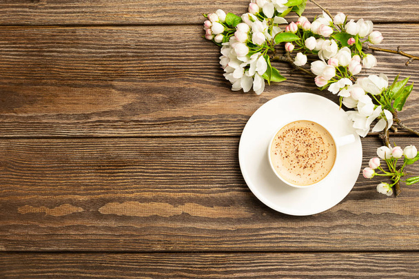 A cup of hot aromatic coffee and a blossoming branch of an apple tree on a wooden background. Flat layout. - Photo, Image