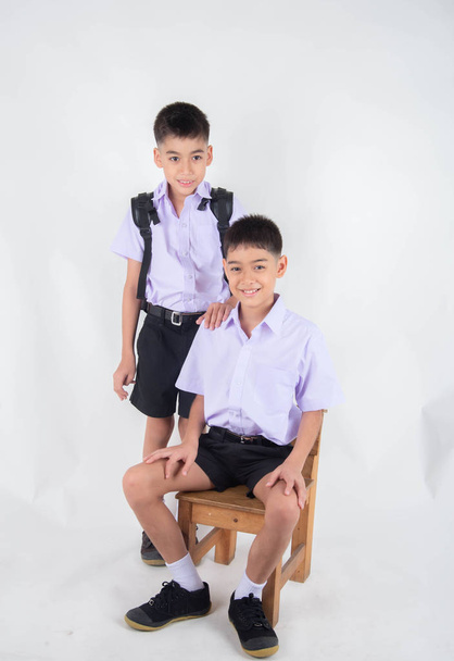 kleine asiatische Geschwister Jungen in Studentenuniform posieren zusammen auf weißem Hintergrund - Foto, Bild
